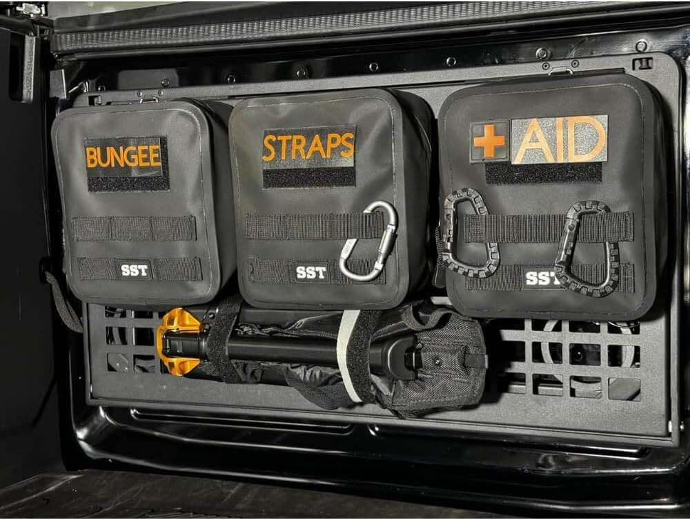Closed storage compartments labeled Bungee, Straps, and Aid attached to a vehicle interior, designed for tactical organization.